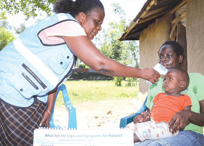 A community health worker takes a child’s body temperature during a past visit to a family’s home. PHOTO/Print