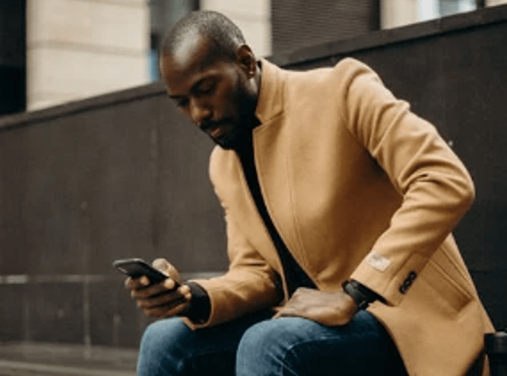 Man sat on the sidewalk busy on his phone. Image used for illustration purposes. PHOTO/Pexels