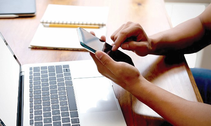 Browsing on the phone and a laptop on the desk. PHOTO/PRINT