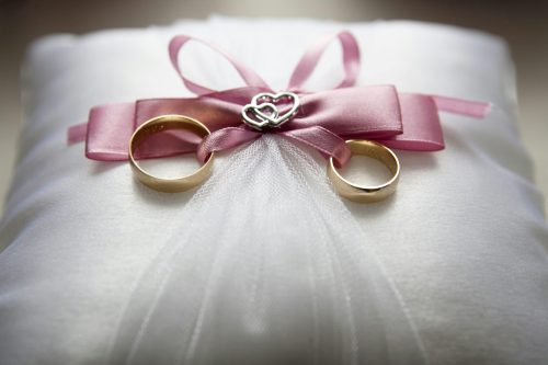 Silver-colored engagement ring set with pink bow accent on throw pillow. Image used for representational purposes only. PHOTO/Pexels