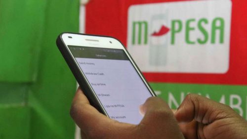 A person using their phone in front of an M-Pesa shop. Image is used for illustration. PHOTO/@TerryanneChebet/X